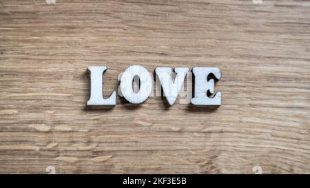 Love - word inscription of 3D wooden letters on the wood textured board background. Expression of romantic theme or Valentines Day. Rustic style inscription. Stock Photo