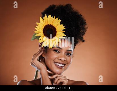 Flower, beauty and woman or portrait for skincare, haircare and natural health or wellness. Sunflower, nature and black woman on a brown studio Stock Photo