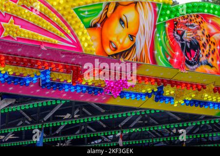 Detail of bright neon lights at outdoor fair ride with female & leopard illustrations & golden shooting stars. Stock Photo