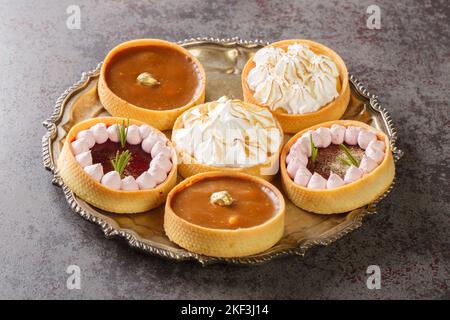 Festive dessert of tartlets with meringue and lemon curd, raspberry mousse, nuts and chocolate close-up on a plate on the table. Horizontal Stock Photo