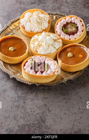 Beautiful tartlets with meringue and lemon curd, raspberry mousse, nuts and chocolate close-up on a plate on the table. Horizontal Stock Photo