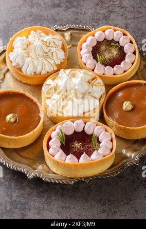 set of sweet tartlets for the holiday with lemon curd, raspberry curd, nuts and chocolate close-up on a plate on the table. Vertical Stock Photo