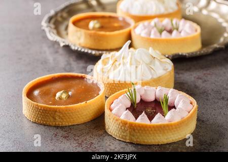 Delicious gourmet sweets tartlets for the holiday with meringue and lemon curd, raspberry curd, nuts and chocolate close-up on the table. Horizontal Stock Photo