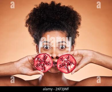 Black woman beauty, pomegranate and face in skincare portrait with fruit in by orange background. African model, woman and cosmetics studio for health Stock Photo