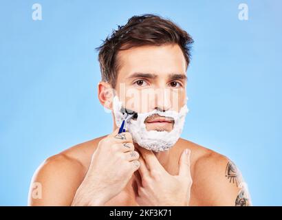 Portrait, shave and razor with a man model grooming in studio on a blue background for wellness or care. Face, skin and shaving with a handsome young Stock Photo