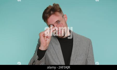 Need some more, please give me. Business man showing a little bit gesture with sceptic smile, showing minimum sign, measuring small size, asking for help. Young guy isolated on blue studio background Stock Photo