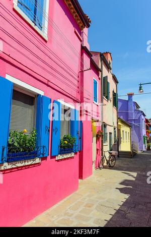 Flower pots decorate on the walls and blue windows of the pink house. Colorful architecture in Burano Island, Venice, Italy Stock Photo