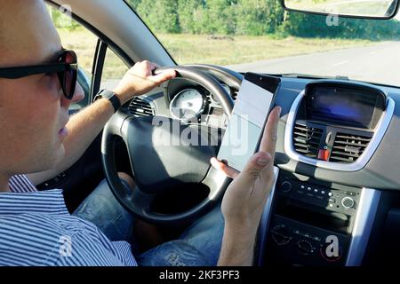 Holding a steering wheel and using a mobile phone.Close-up of a man's hand holding a smartphone. Businessman texting while sitting in a car. Stock Photo
