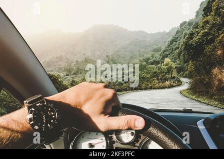 A man rides on a mountain road serpentine. Beautiful road between the hills. Driving a car on mountain road. View of mountains through windscreen. Stock Photo