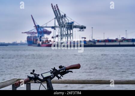 Handlebar of a black electric bicycle leaning against a parapet in Hamburg, blurred background with the Elbe river and container cranes, selective foc Stock Photo