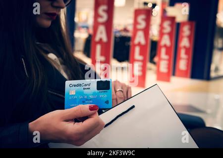 Attractive woman with credit card and shopping bag at red sale signs background. Lady doing shopping during total discounts season. Paying for purchas Stock Photo