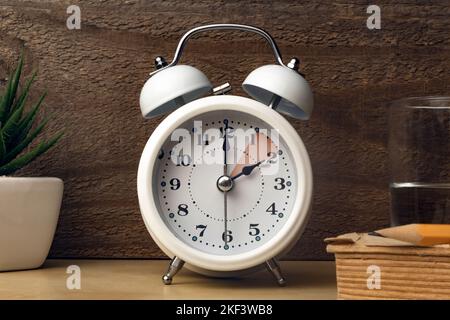 Daylight saving time concept: an alarm clock placed on a bedside table with an indication to move the hands backward Stock Photo