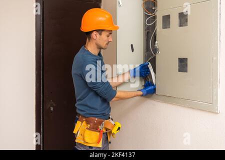 Close up shot of hand of aged electrician repairman in uniform working, fixing, installing ethernet cable in fuse box, holding flashlight and cable Stock Photo