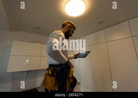 Installation lighting. Builder is holding a tablet in his hands. Concept - lighting engineer. Process installing. Electrician Stock Photo