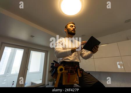 Installation lighting. Builder is holding a tablet in his hands. Concept - lighting engineer. Process installing. Electrician Stock Photo