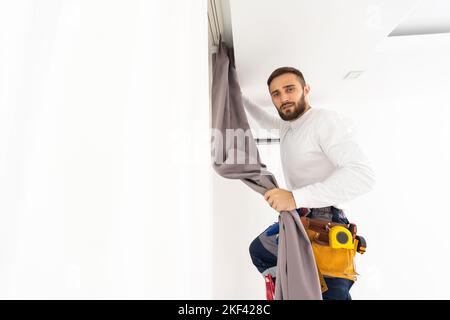 Man hanging window curtain indoors. Interior decor element Stock Photo