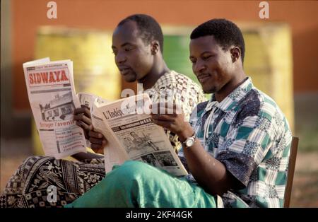 Burkina Faso. Men are reading a newspaper sitting on a public bench in Ouagadougou. Stock Photo