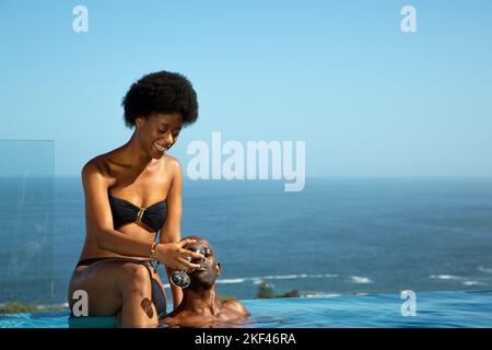 A young African couple chilling in a pool under the clear blue sky Stock Photo
