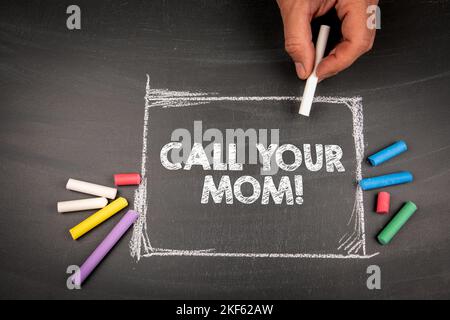 Call Your Mom. Text and colored pieces of chalk on a dark blackboard. Stock Photo