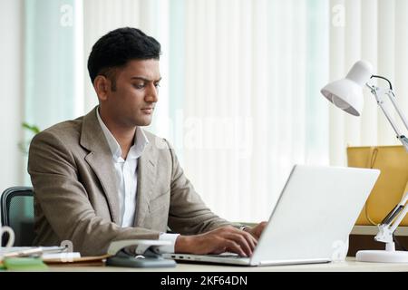 Portrait of serious Indian entrepreneur working on laptop in office Stock Photo