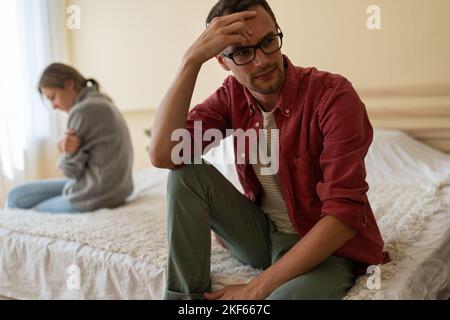 Young unhappy family couple sitting separately on bed at home, having problems in relationship Stock Photo