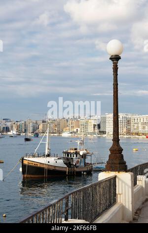 Sliema, Malta - November 12, 2022: Waterfront promenade with moored boats on cloudy morning Stock Photo