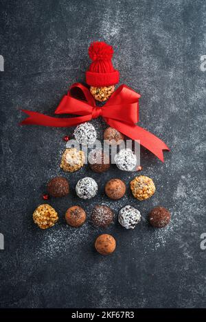 Christmas tree made of chocolate truffles, hazelnuts, anise stars, decorations, spoons and powdered sugar snow on dark background. Christmas holiday c Stock Photo