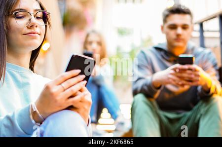 Group of friends using cellphones -  Students sitting in a stairs and typing on the smartphones Stock Photo