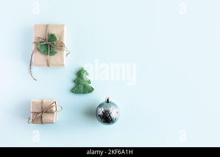 Christmas composition of a gift box in gray craft paper decorated with a knitted green Christmas tree and a Christmas ball on a green background, the Stock Photo