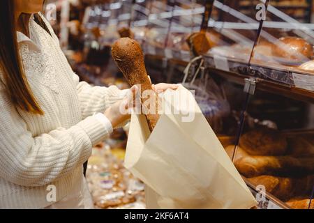 Woman in Bakery Putting Freshly Baked Organic Sourdough Bread Loaf Into Sustainable Paper Bag Stock Photo