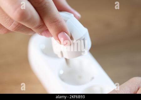 Close-up of woman's hand inserting electric plug into socket. Stock Photo