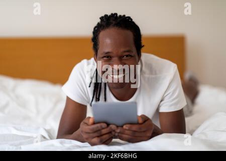 Cheerful Young Black Man With Digital Tablet Resting In Bed At Home Stock Photo