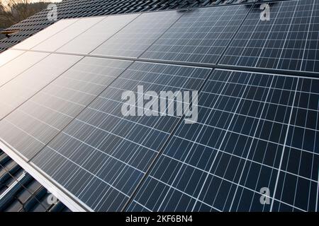 New solar panels are mounted on a roof with shiny black tiles and the clear sky is reflected in the warm sunlight in it. Stock Photo