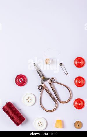 A composition of red sewing thread, thimble, vintage scissors, buttons and safety pin on a white background Stock Photo