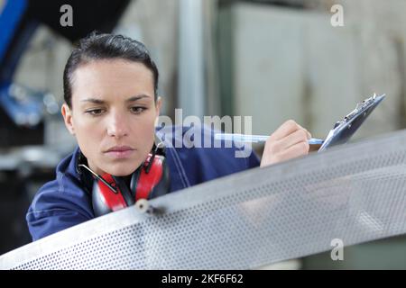 woman with clipboard inspecting industrial metal component Stock Photo