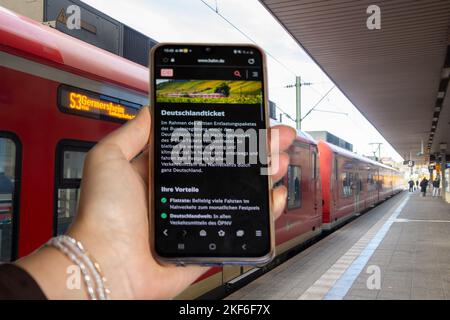 Symbol image Deutschlandticket, 49-Euro-Ticket: Close-up of a smartphone in front of passengers boarding and disembarking at a train stop Stock Photo