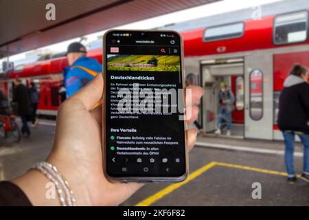 Symbol image Deutschlandticket, 49-Euro-Ticket: Close-up of a smartphone in front of passengers boarding and disembarking at a train stop Stock Photo