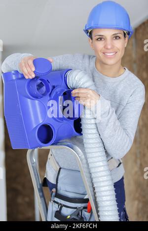 female worker fitting ventilation hose into roof space Stock Photo
