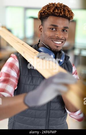 young male worker carrying tied wooden planks at construction site Stock Photo