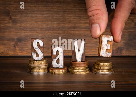 Save concept. Text and coins on wooden background. Stock Photo