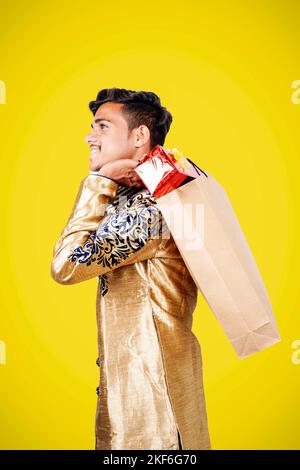 Indian man in ethnic wear with shopping bags and gift box, isolated over yellow background Stock Photo