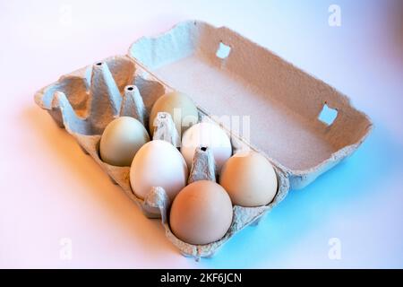 Fresh two light brown, two white and two light green eggs in a paper box and four empty spaces for healthy food. Egg container made of recyclable mate Stock Photo