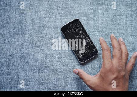 hand reaching from a broken smart phone on table  Stock Photo