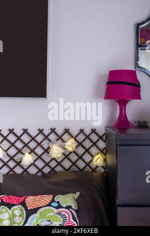 Corner of a bedroom with cushions, a chest of drawers in dark color and a pink lamp Stock Photo