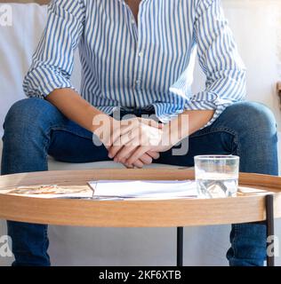 Unrecognizable young man sitting in the sofa with shirt on and held hands with papers and documents on the wooden table Stock Photo