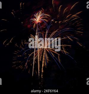 Two large exploding fireworks and a streak of a third one, isolated on a black sky, during a celebration display. Stock Photo