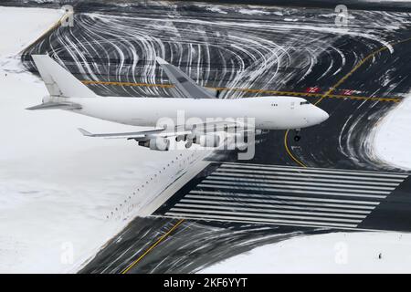 White aircraft landing on airport runway during winter day. Large unidentified airplane for cargo before landing. Four engines plane from above. Stock Photo