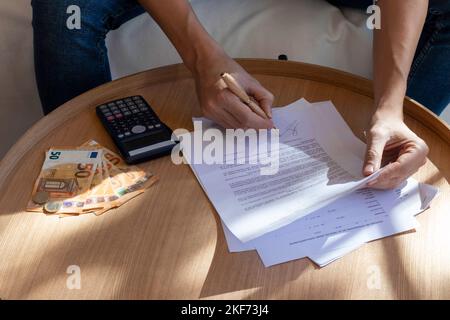 Unrecognizable man signing contract document on a wooden table with a pen. Calculator, money bills in euro currency Stock Photo