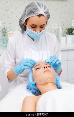 beautician applies the mask to the face of beautiful woman Stock Photo