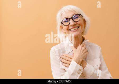 Beautiful smiling senior woman with folded arms on her chest over brown isolated background Stock Photo